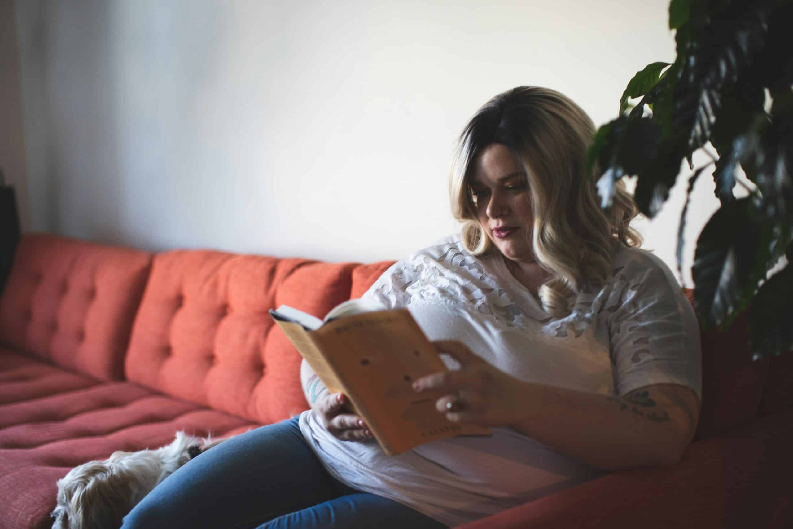 an obese woman sitting on a red sofa and reading a book