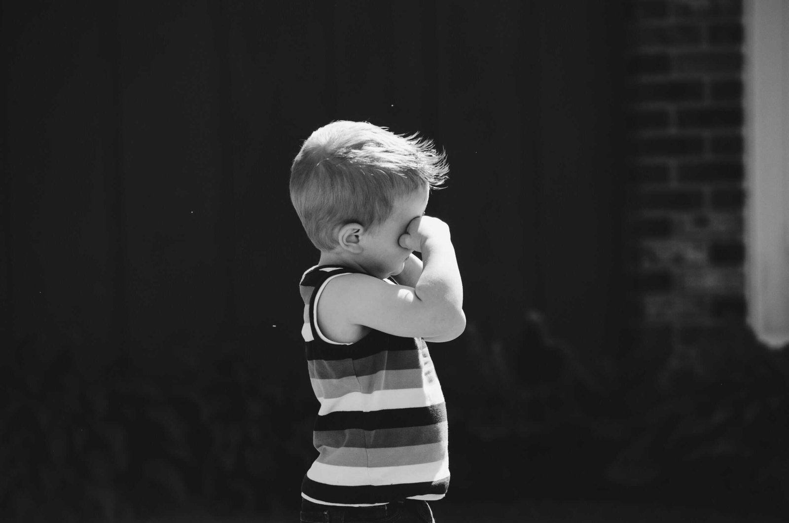 A young boy is standing in front of a brick building.