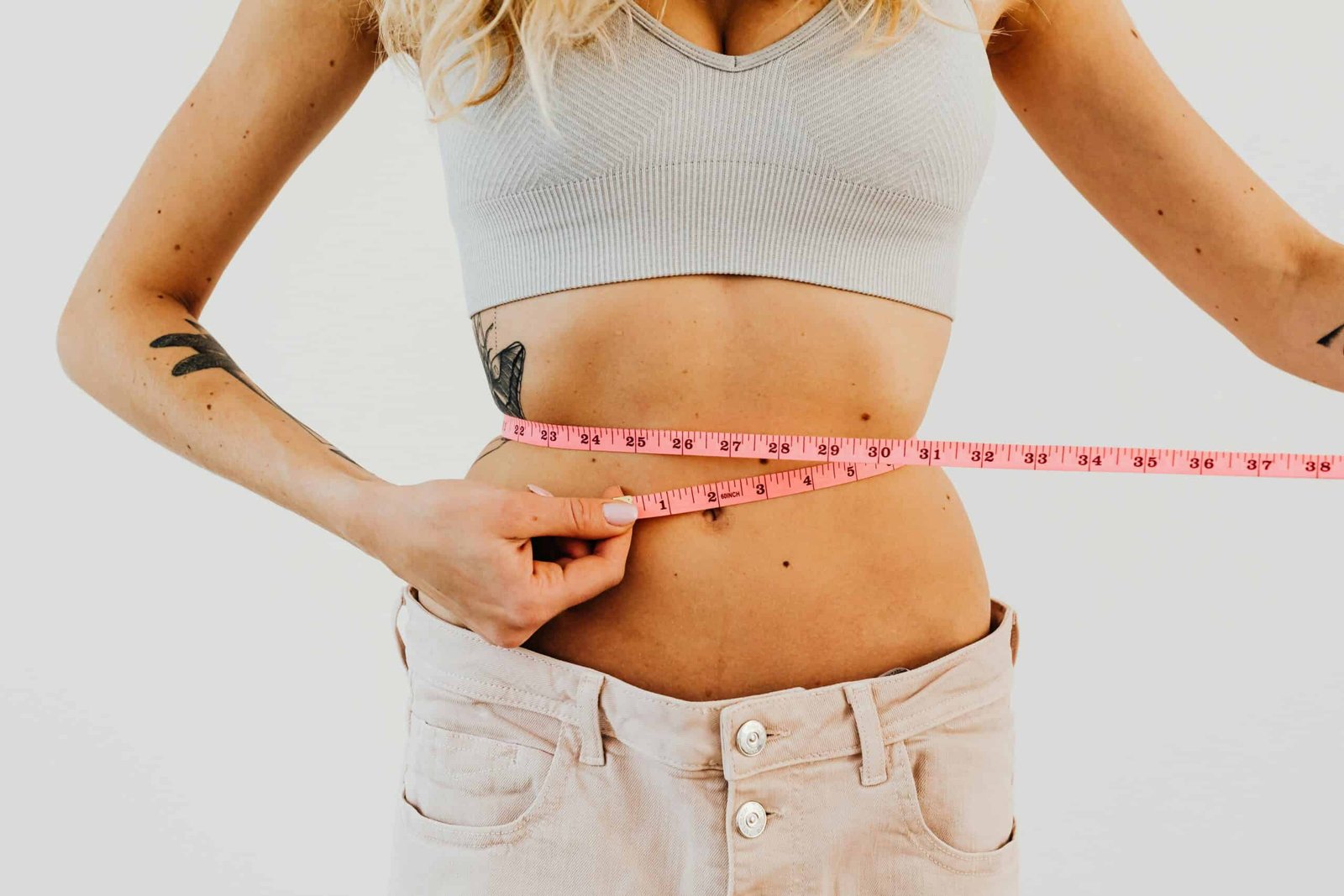 A woman measuring her waist with a pink tape.