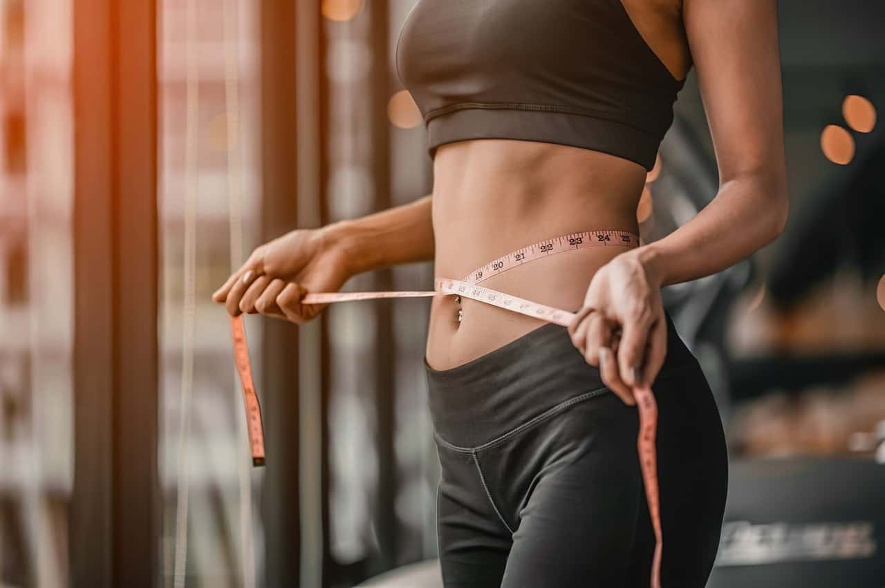 A woman is measuring her waist with a tape.